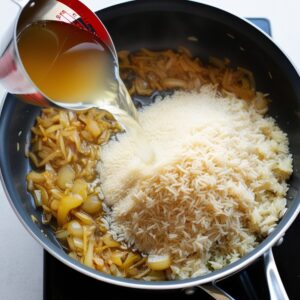 Rinsed rice and vegetable stock being added to sautéed onions in a saucepan, ready for simmering.