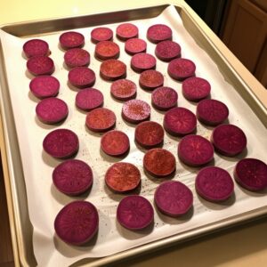 Round slices of seasoned purple sweet potatoes spread evenly on a parchment-lined baking sheet, ready for roasting.