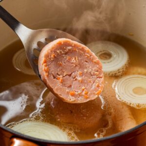 A slotted spoon lowering an oval fish patty into a pot of simmering poaching liquid.